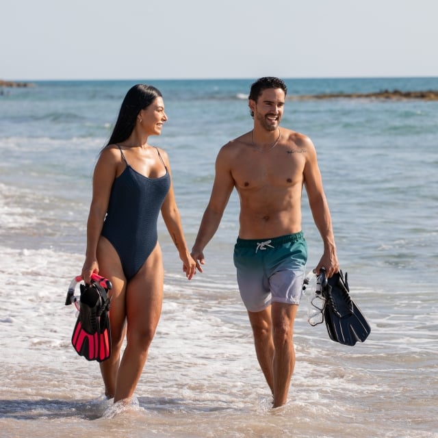 couple strolling on the beach with snorkel gear in hand